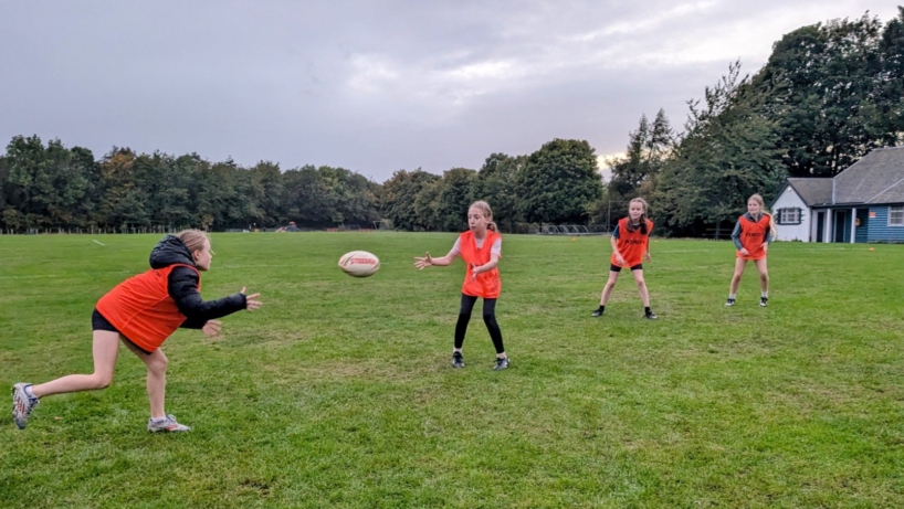 Four young players in orange bibs practising passes on a grass pitch at a Pentland Touch session