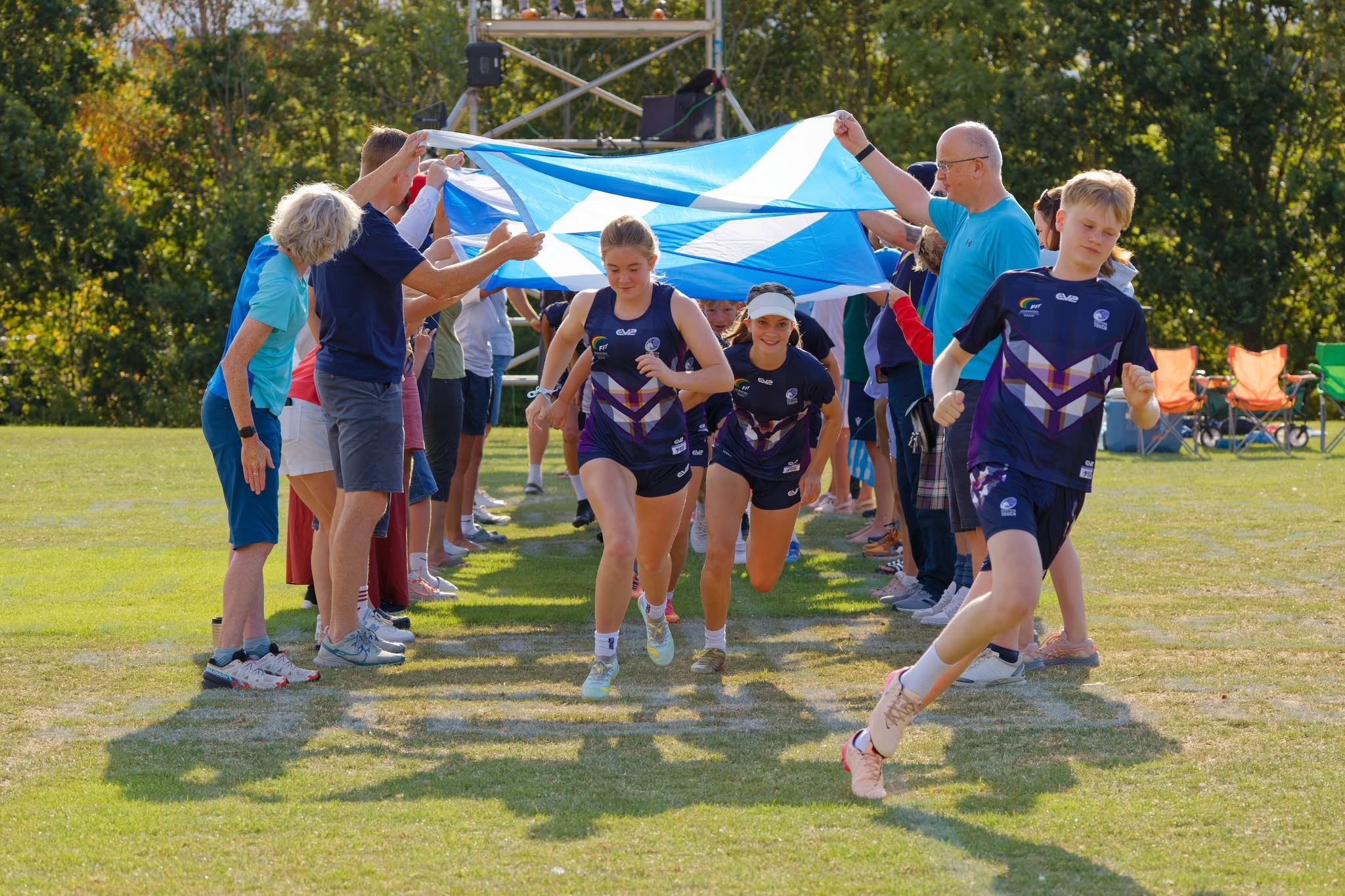 Scotland players in navy and purple kit run out through a tunnel of supporters holding a large saltire flag above them